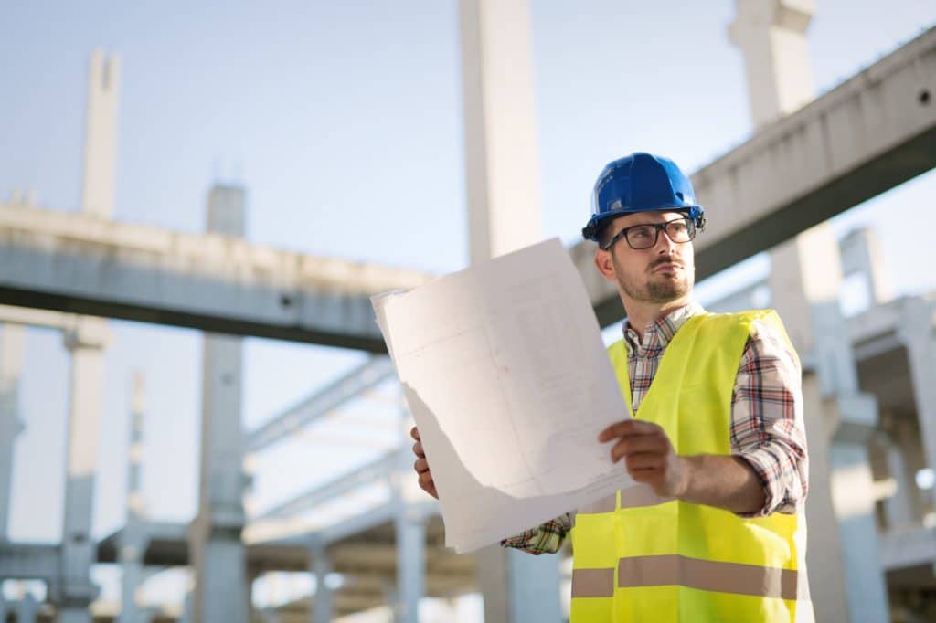 Portrait of male site contractor engineer with hard hat holding blue print paper