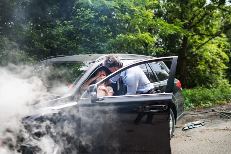 A man helping a young woman to get out of the car after a car accident.