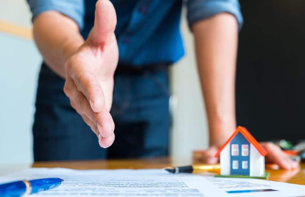 Home salesman stretches to shakes hands, Pen and model house on house plan.