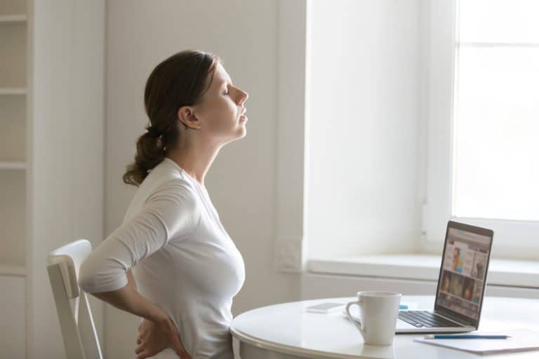 Profile portrait of a woman at desk stretching, backache position