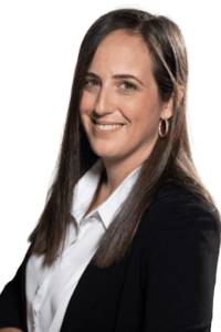 Smiling woman with long dark hair wearing a white blouse and black blazer. She has hoop earrings and is posed at a slight angle against a light background.