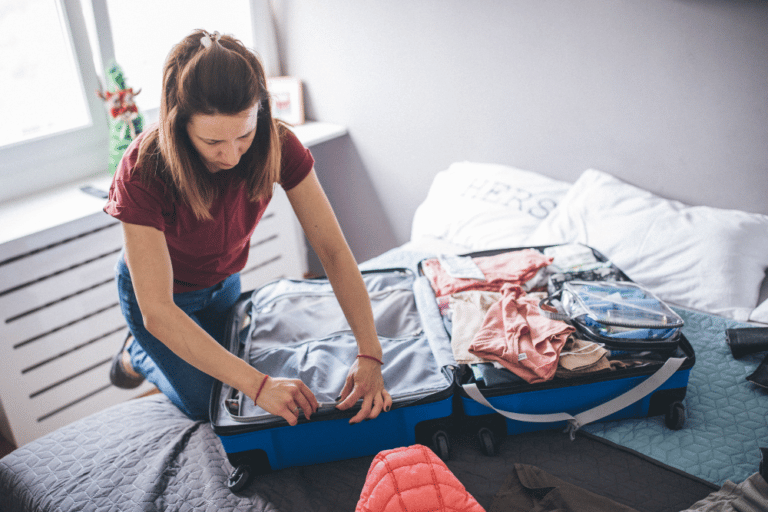 A woman is putting clothes into a suitcase on a bed.