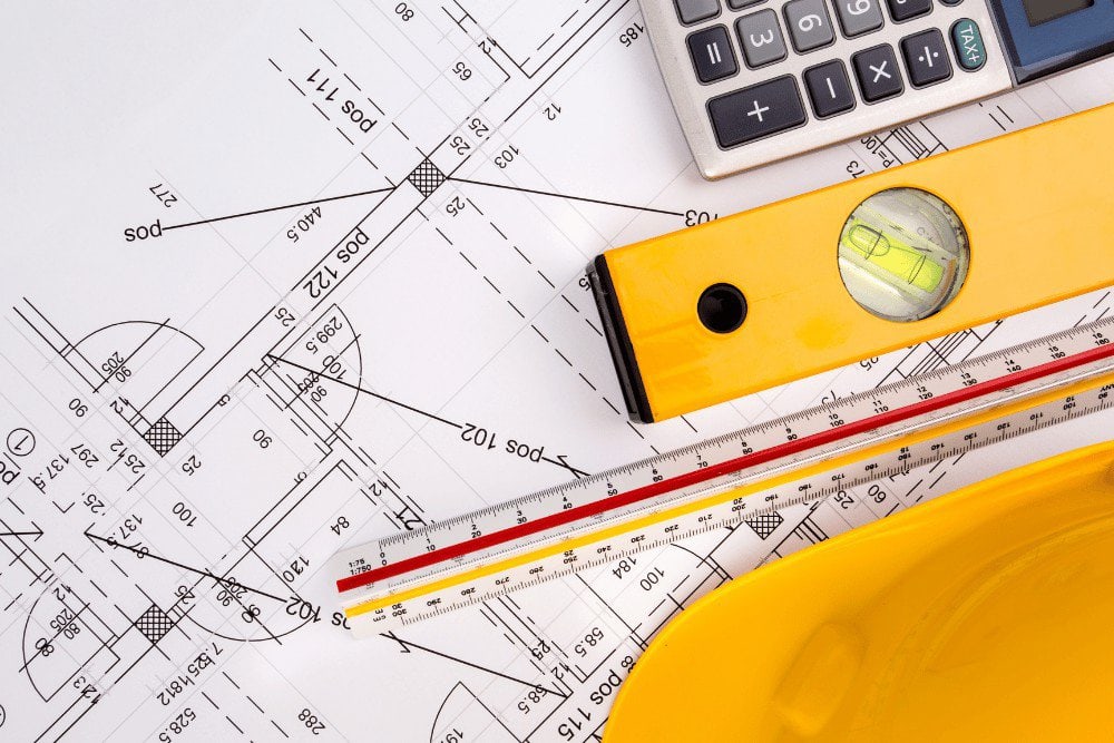 A yellow hard hat, a ruler and a calculator on top of blueprints.