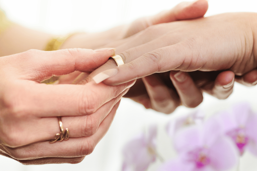 A woman is putting a wedding ring on a woman's hand.