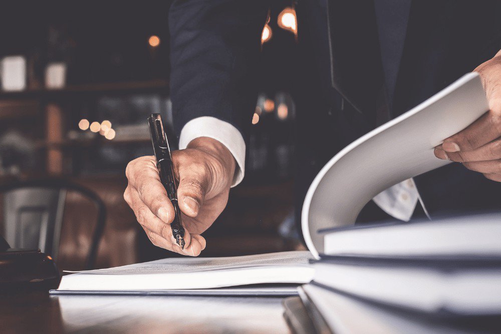 A man in a suit writing on a book.