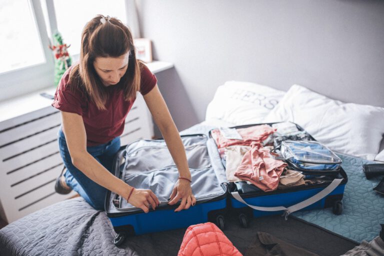 A woman is putting clothes into a suitcase on a bed.