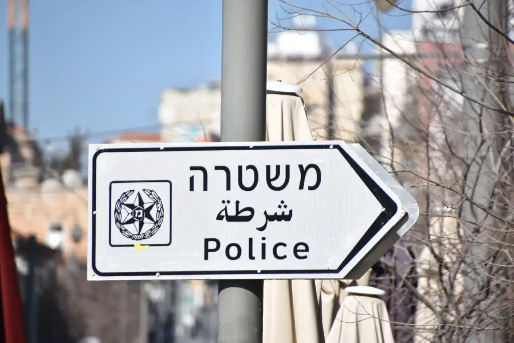 שלט רחוב המותקן על עמוד מצביע על תחנת, בעברית, ערבית ואנגלית, האומר משטרה, יחד עם סמל. ברקע נראה