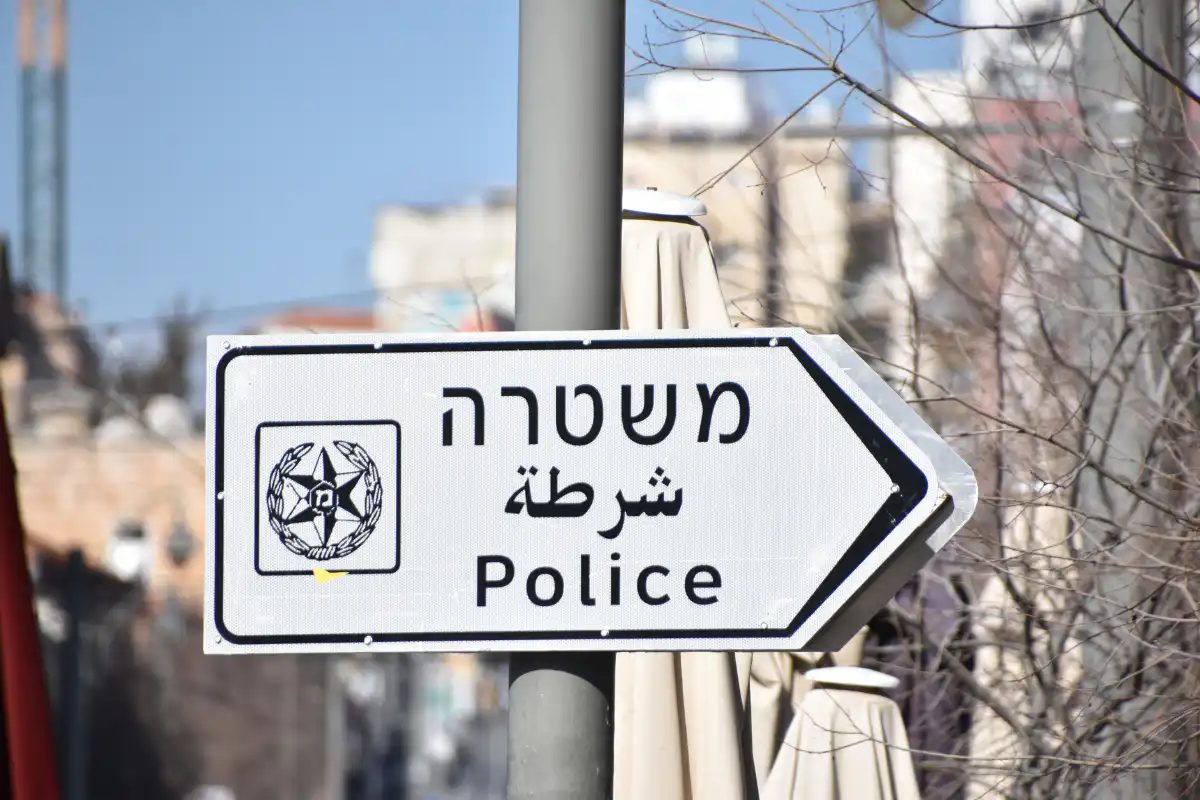 שלט רחוב המותקן על עמוד מצביע על תחנת, בעברית, ערבית ואנגלית, האומר משטרה, יחד עם סמל. ברקע נראה