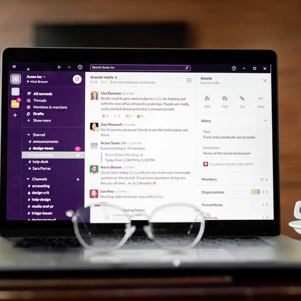מחשב נייד המציג סביבת עבודה של Slack נמצא על שולחן, עם זוג משקפיים מלפנים. המסך מציג שיחה