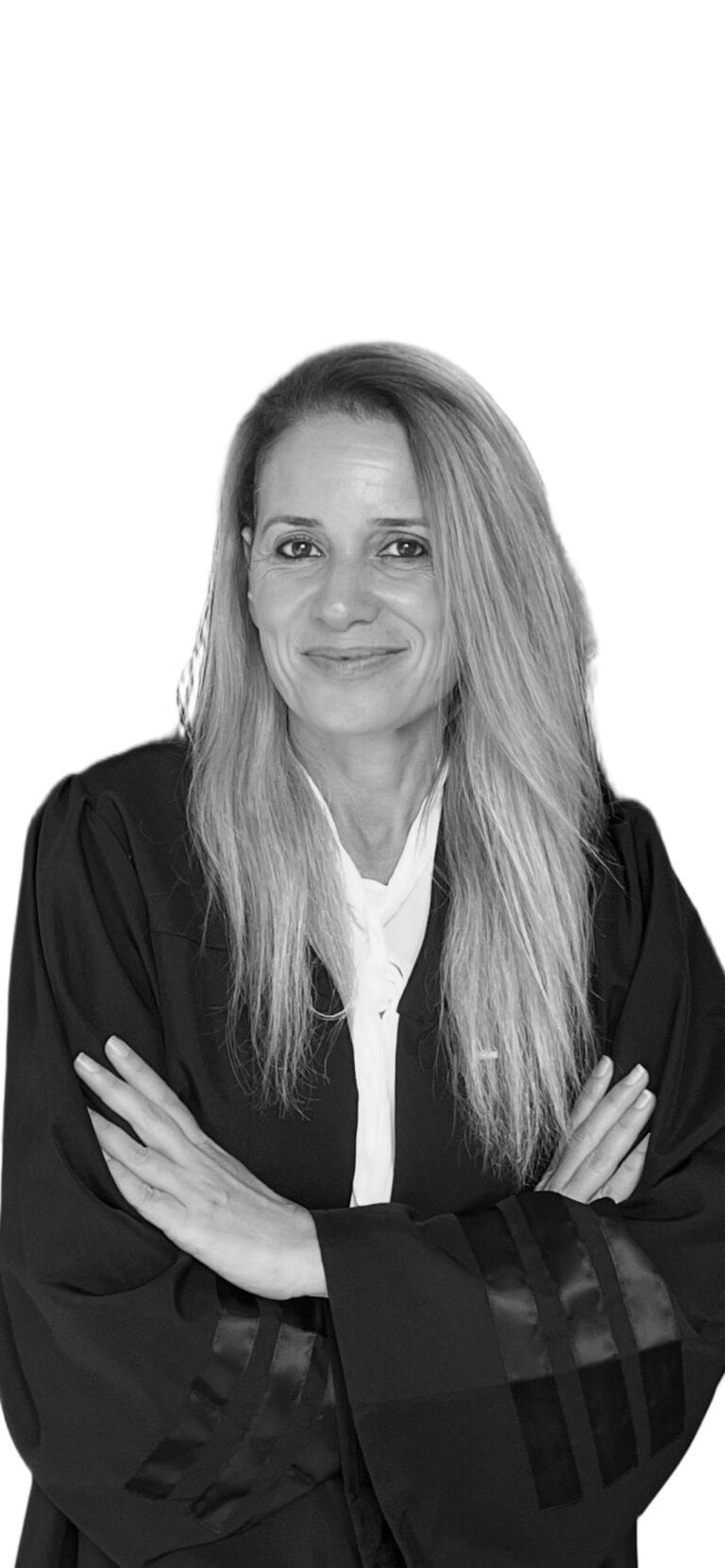 אישה עם שיער ארוך ובהיר, לבושה בגלימה שחורה וחולצה לבנה, עומדת בזרועות שלובות, מחייכת בביטחון על רקע לבן.