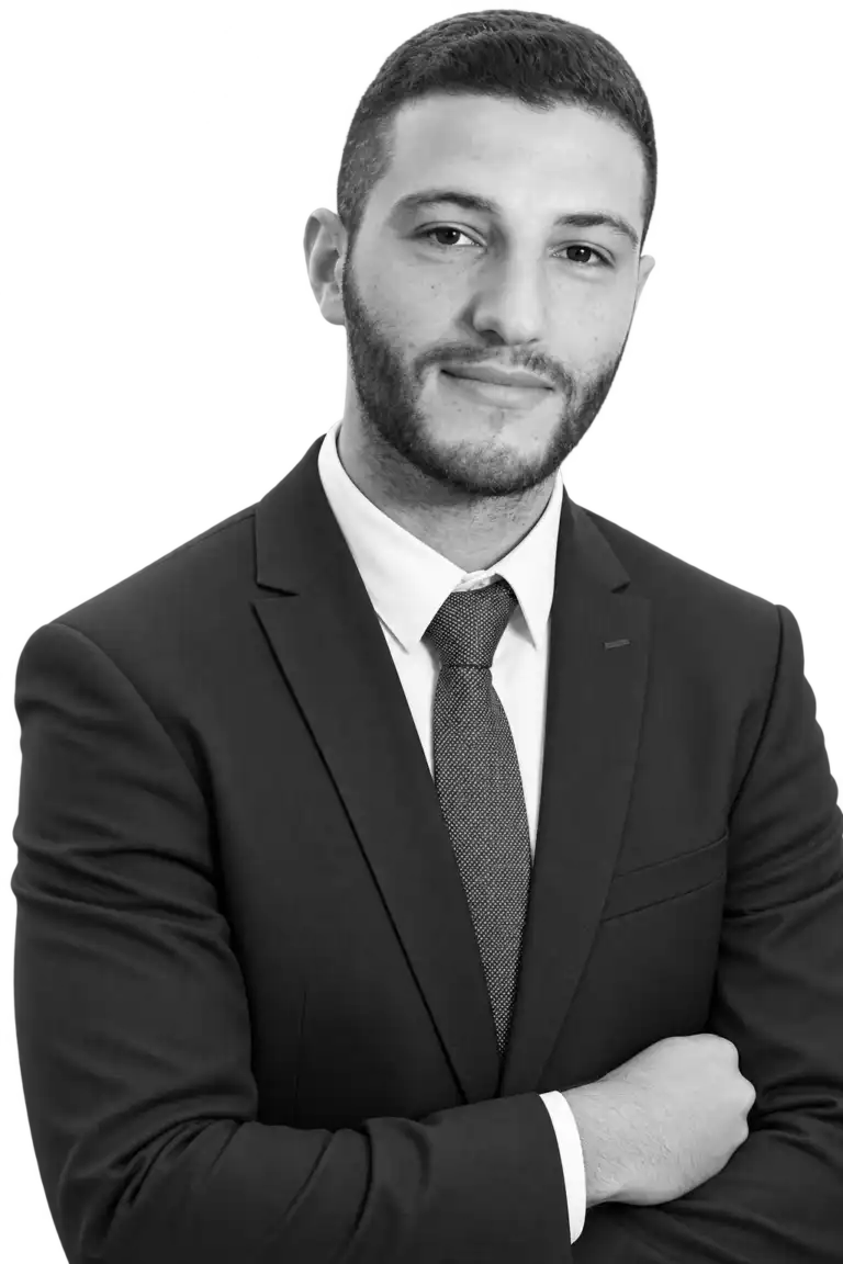 Professional headshot of a man in a dark suit and tie with arms crossed, looking at the camera (black-and-white).