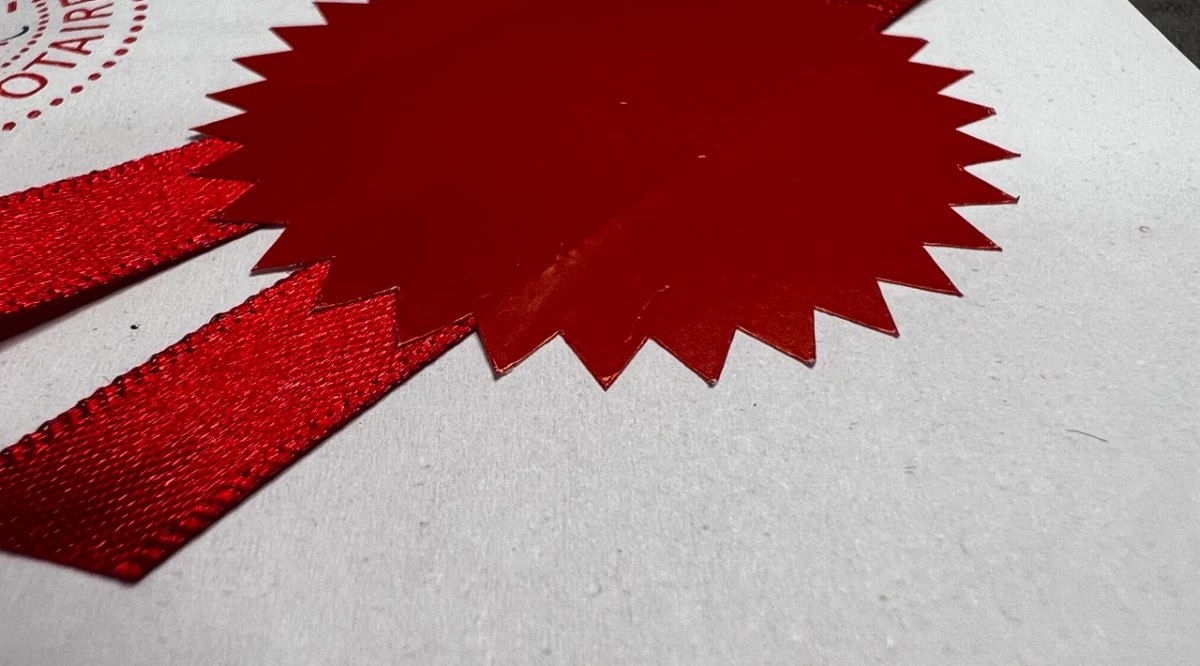 A red notarial seal and ribbon resting on a certificate